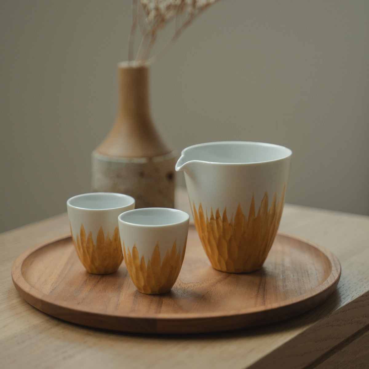White and gold Japanese sake carafe and sake cups on a wooden tray, welcoming guests to a bright Japandi dining space.