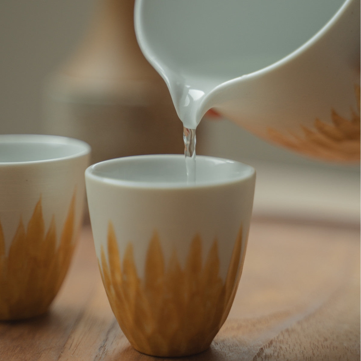 Pouring clear sake from a white and gold Japanese sake pitcher into a cup, elevating a celebratory dinner for guests.