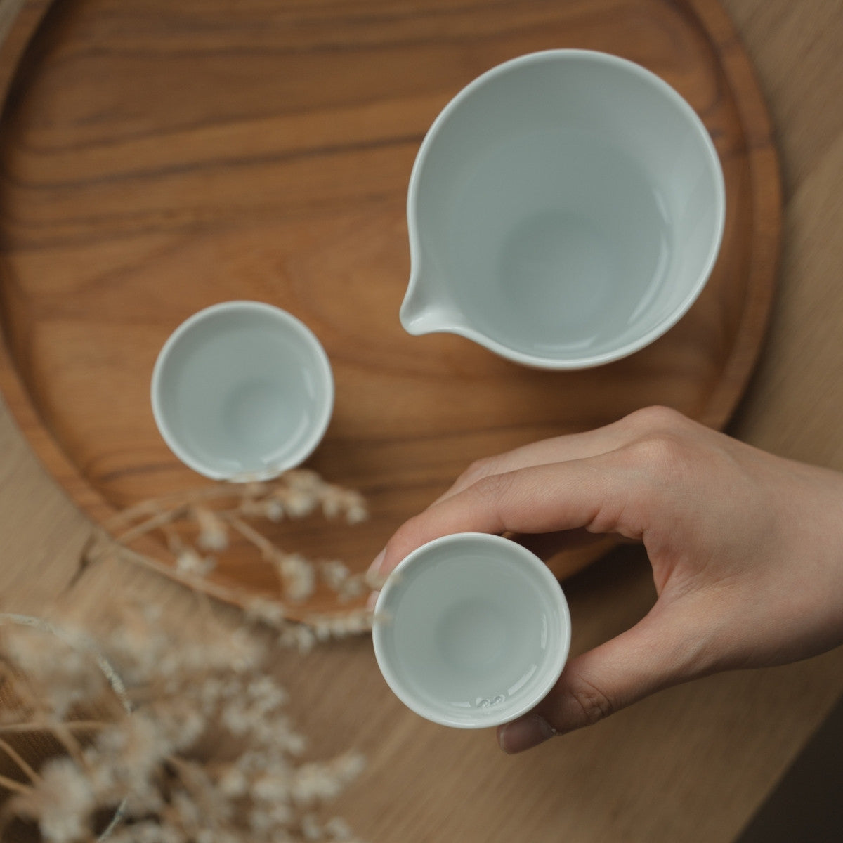 Hand holding a white arita porcelain sake cup over a tray, preparing sake lovers for a mindful and elegant evening.