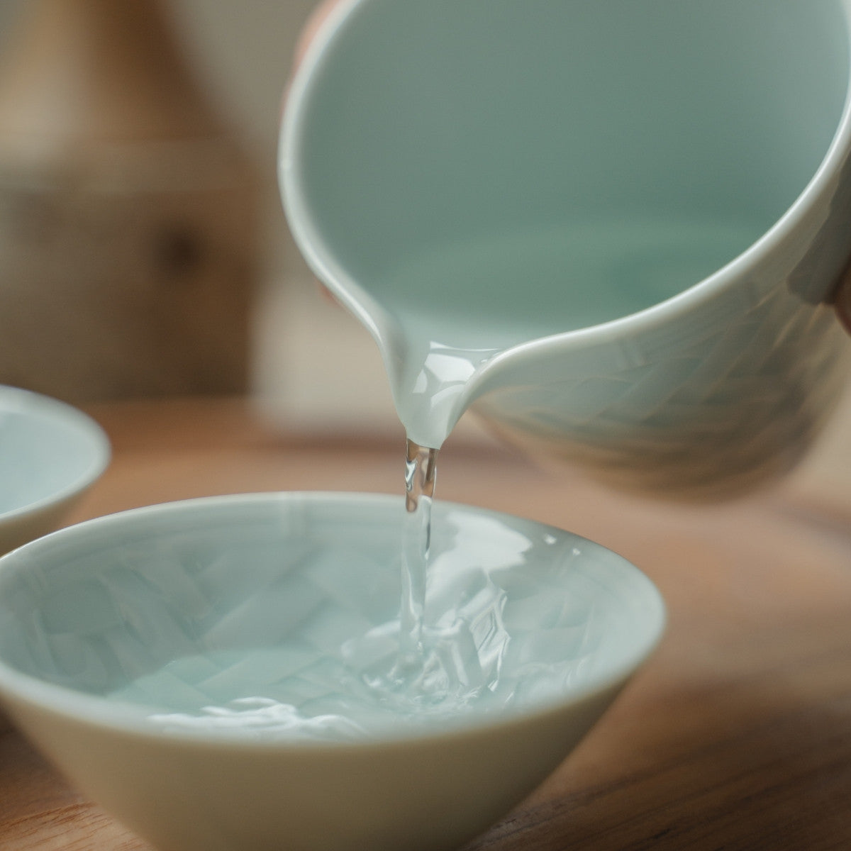 Hand pouring from an ice blue Japanese sake carafe into a textured sake cup, elevating a special dinner gathering.