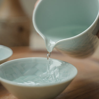 Hand pouring from an ice blue Japanese sake carafe into a textured sake cup, elevating a special dinner gathering.