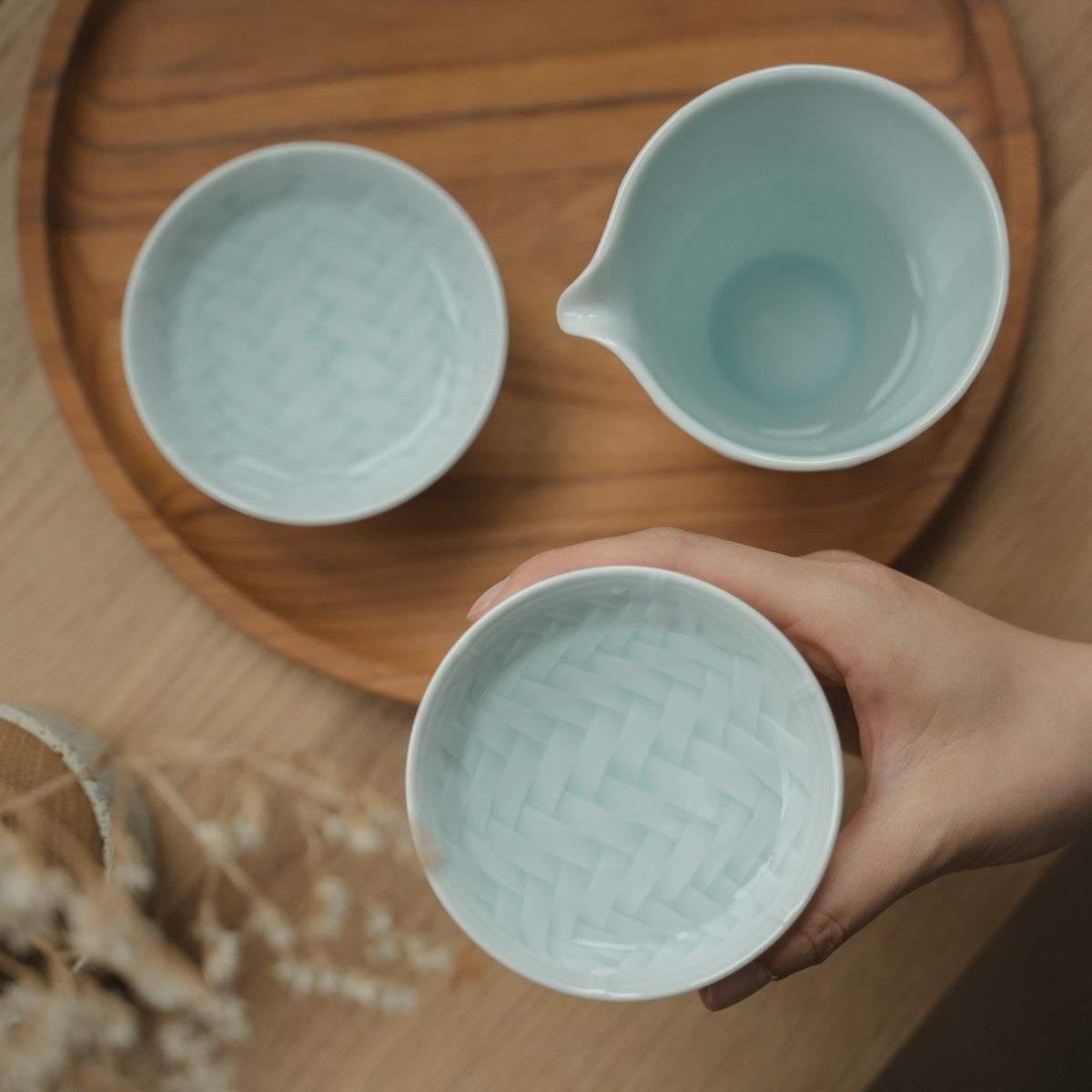 Hand holding an ice blue Japanese arita porcelain guinomi over a tray, inviting sake lovers to enjoy a tranquil evening.