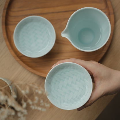 Hand holding an ice blue Japanese arita porcelain guinomi over a tray, inviting sake lovers to enjoy a tranquil evening.