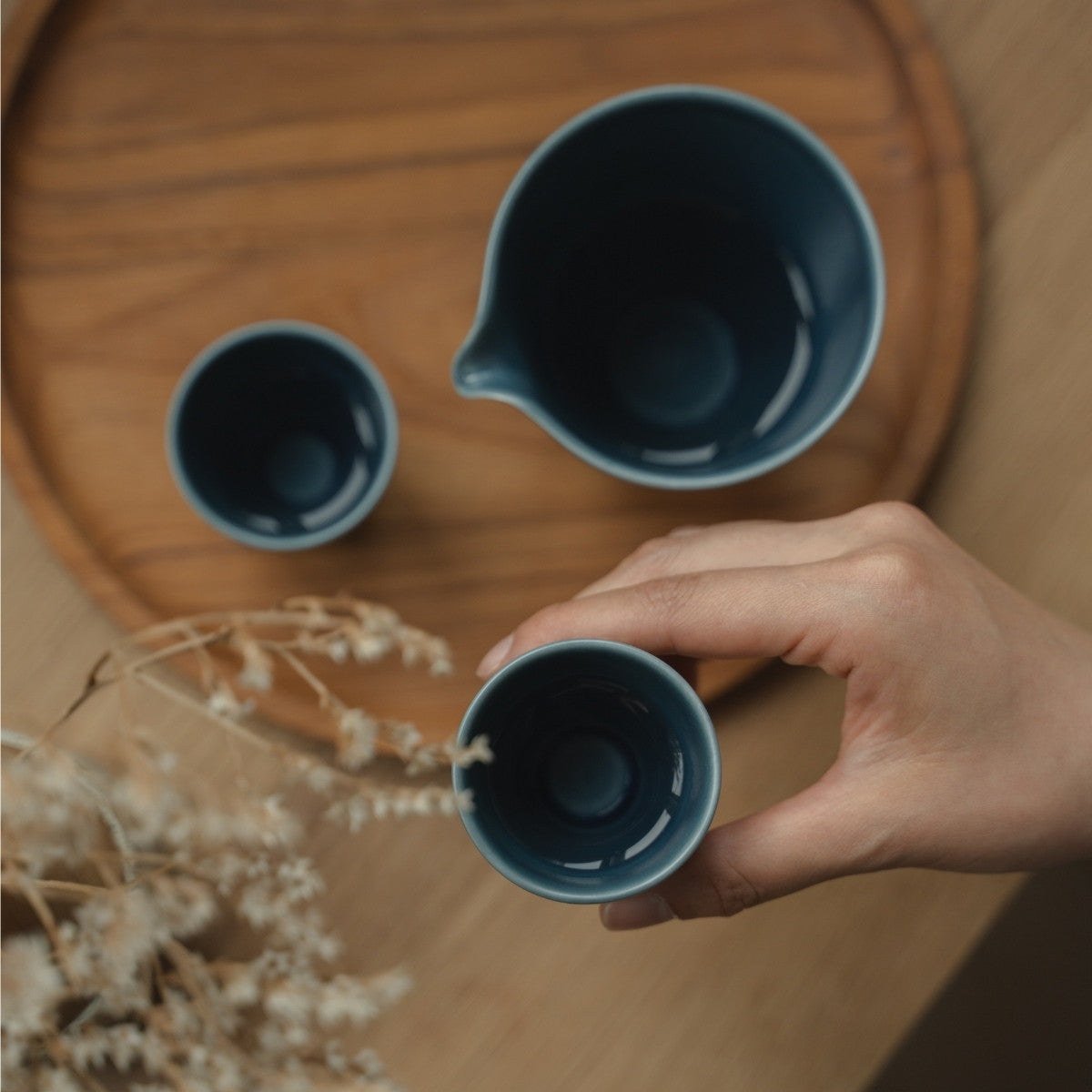 Matte blue arita porcelain guinomi held over a wooden tray, preparing sake lovers for a tranquil evening sake ritual.