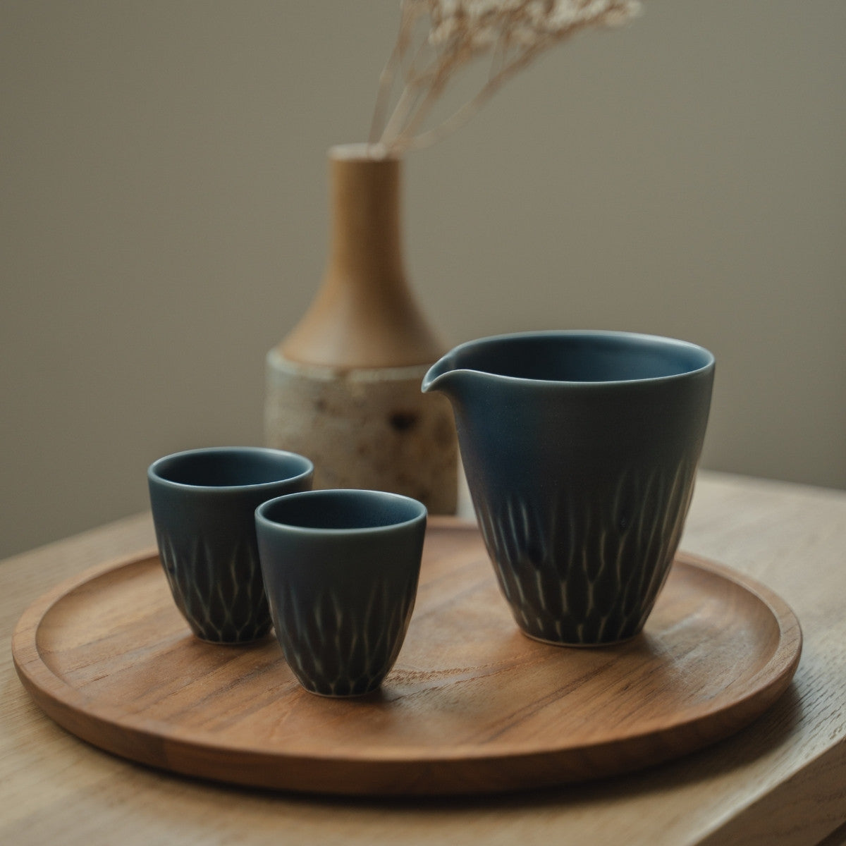Matte blue Japanese sake carafe and sake cups on a wooden tray, welcoming guests to enjoy a mindful modern dining space.