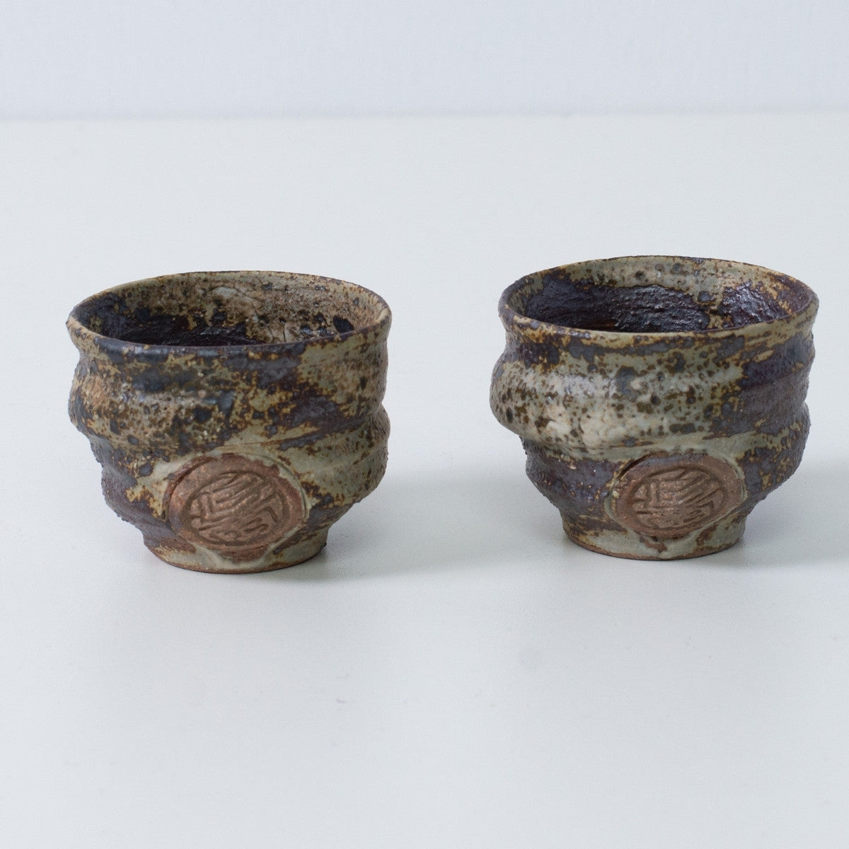 Zwei japanische Sake-Becher Ochoko "Sakigake" in rustikalem Braun, handgefertigt in Japan, mit eingraviertem Siegel des Kunsthandwerkers auf der Vorderseite.