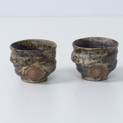 Zwei japanische Sake-Becher Ochoko "Sakigake" in rustikalem Braun, handgefertigt in Japan, mit eingraviertem Siegel des Kunsthandwerkers auf der Vorderseite.