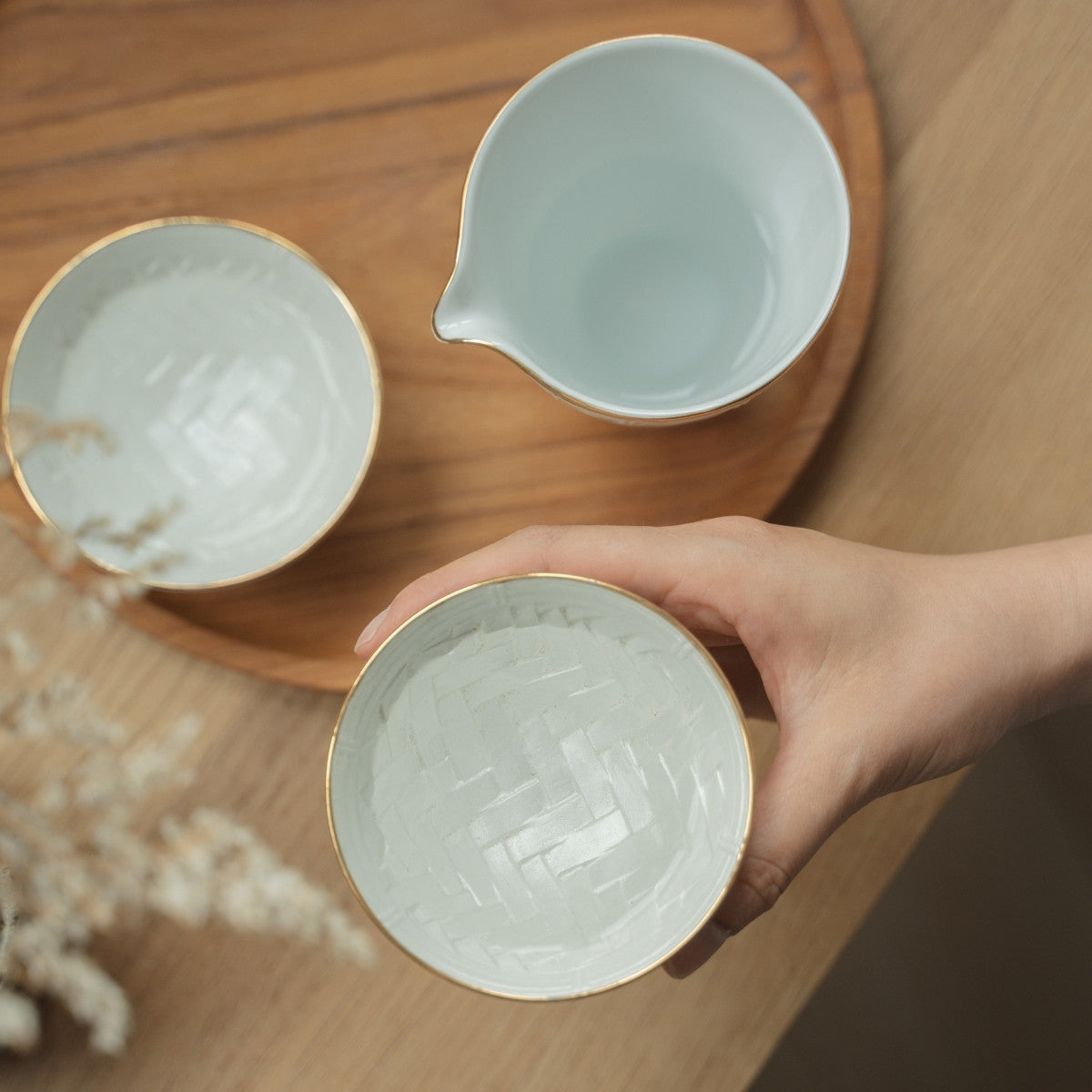 Hand holding a textured white Japanese arita porcelain sake cup over a wooden tray, inviting sake lovers to enjoy a quiet evening.