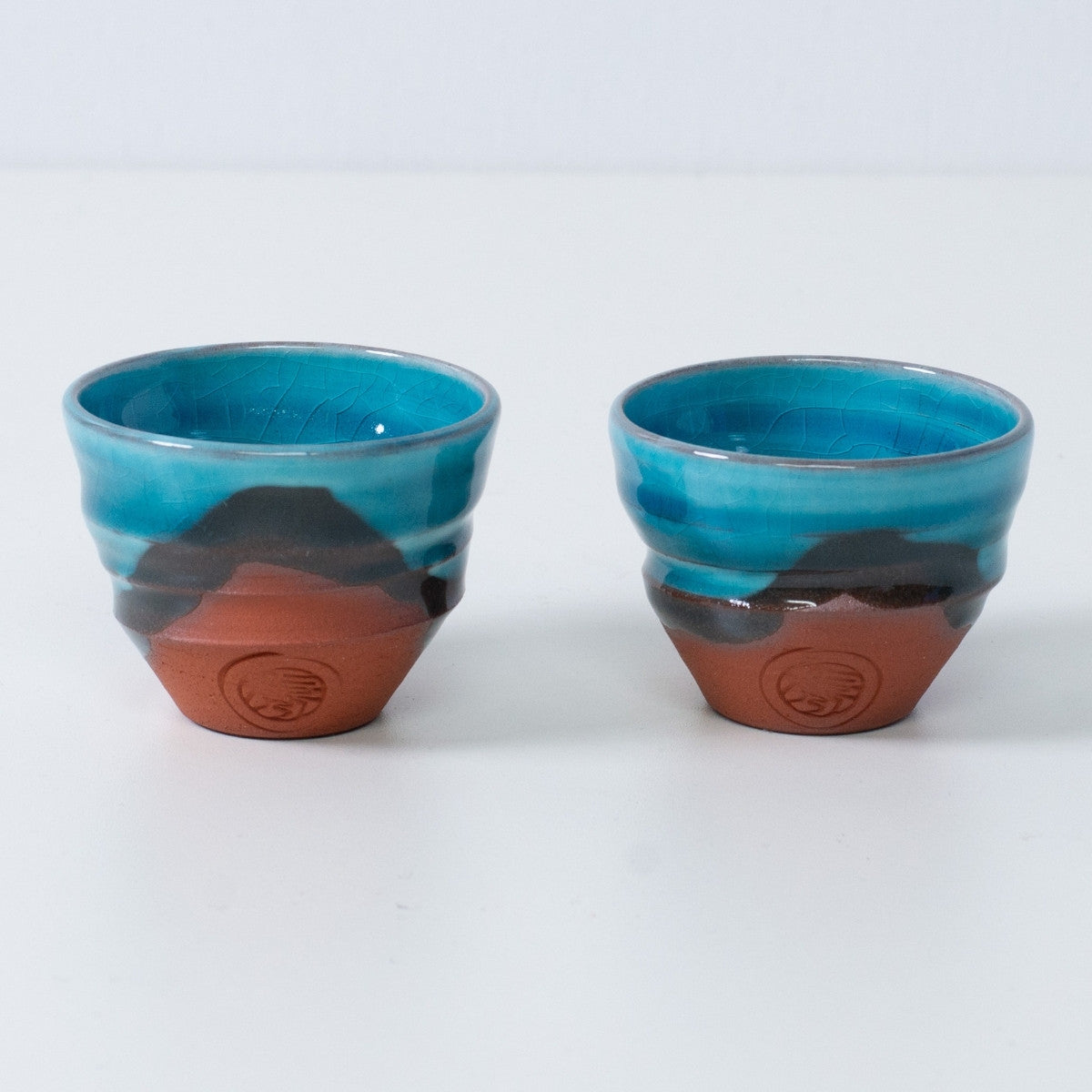 Zwei türkisfarbene japanische Sake-Becher Ochoko "Soku Blue" aus Keramik aus Japan, mit rotem Ton und einem eingravierten Siegel des Kunsthandwerkers auf der Vorderseite.