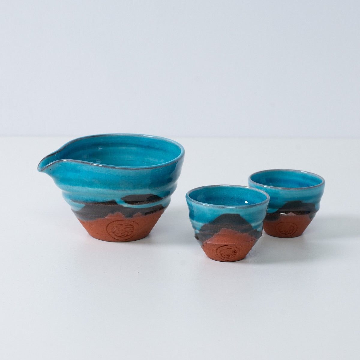 Japanisches Sake-Set "Soku Blue" aus türkisfarbener Keramik mit einem Katakuchi-Sakekrug und zwei kleinen Bechern aus rotem Ton.