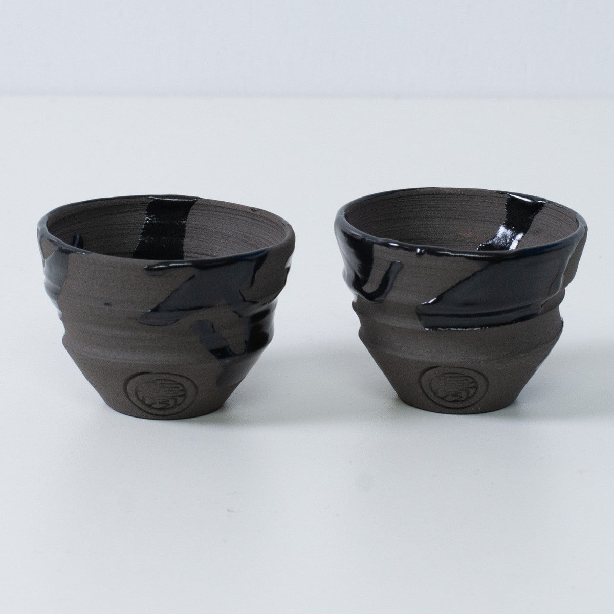 Zwei japanische Sake-Becher Ochoko "Sumi Black" aus Keramik aus Japan, mit eingraviertem Siegel des Kunsthandwerkers auf der Vorderseite jedes Bechers.