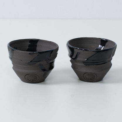 Zwei japanische Sake-Becher Ochoko "Sumi Black" aus Keramik aus Japan, mit eingraviertem Siegel des Kunsthandwerkers auf der Vorderseite jedes Bechers.