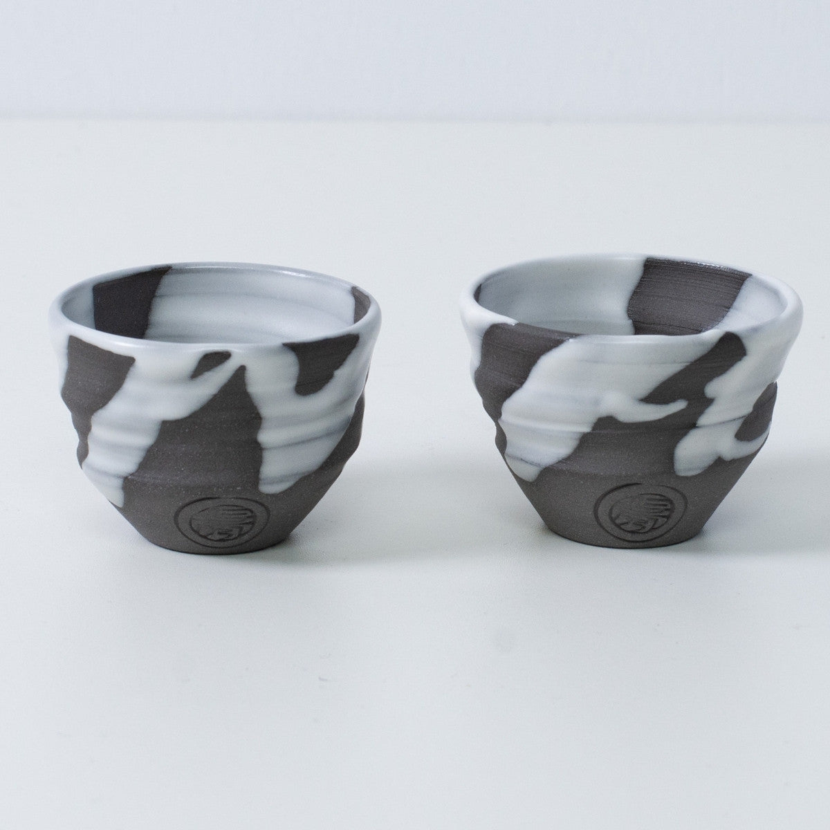 Zwei japanische Sake-Becher Ochoko „White Flow“ aus Keramik aus Japan, mit eingraviertem Siegel des Kunsthandwerkers auf der Vorderseite jedes Bechers.