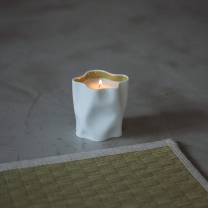 Yuzu japanese scented candle in a white porcelain vessel burning with a soft flame next to a tatami mat.