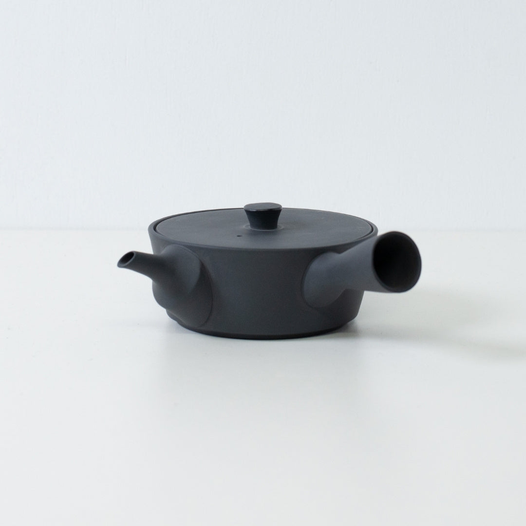 Low profile flat black japanese teapot sencha style with a side handle isolated on a white background.