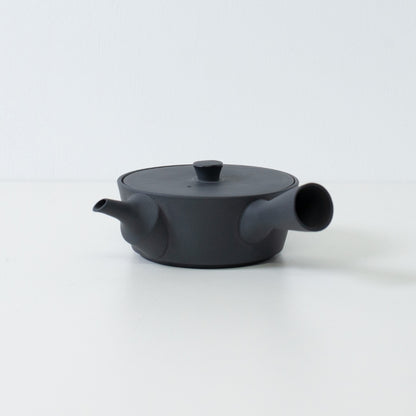 Low profile flat black japanese teapot sencha style with a side handle isolated on a white background.