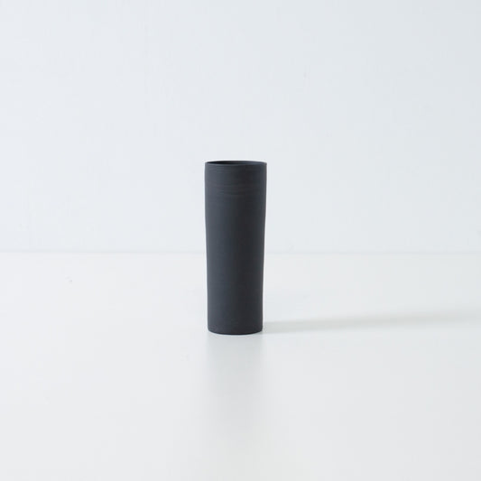 A handcrafted matte black Japanese flower vase in a minimalist cylinder shape for zen ikebana and single blooms.