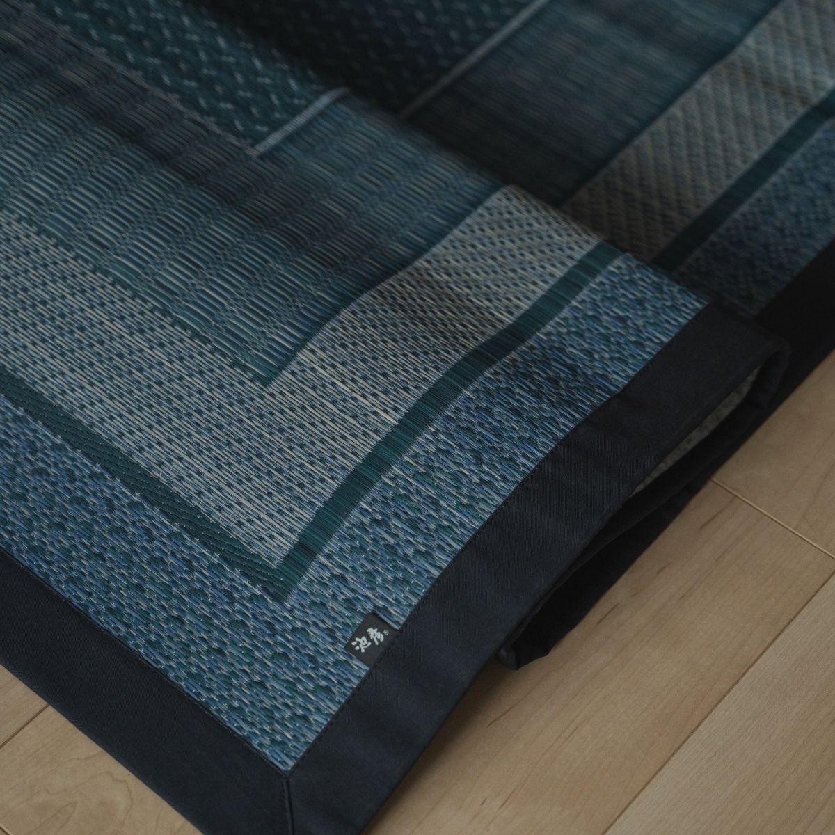 Japanese indigo navy rush tatami area rug folded on a wood floor, offering a geometric pattern for a modern Japanese decor.