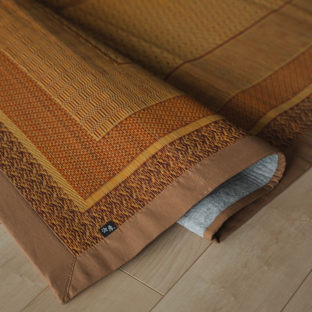 Japanese natural beige rush tatami area rug folded on a wood floor, serving as a stylish tatami mat for Japandi rooms.