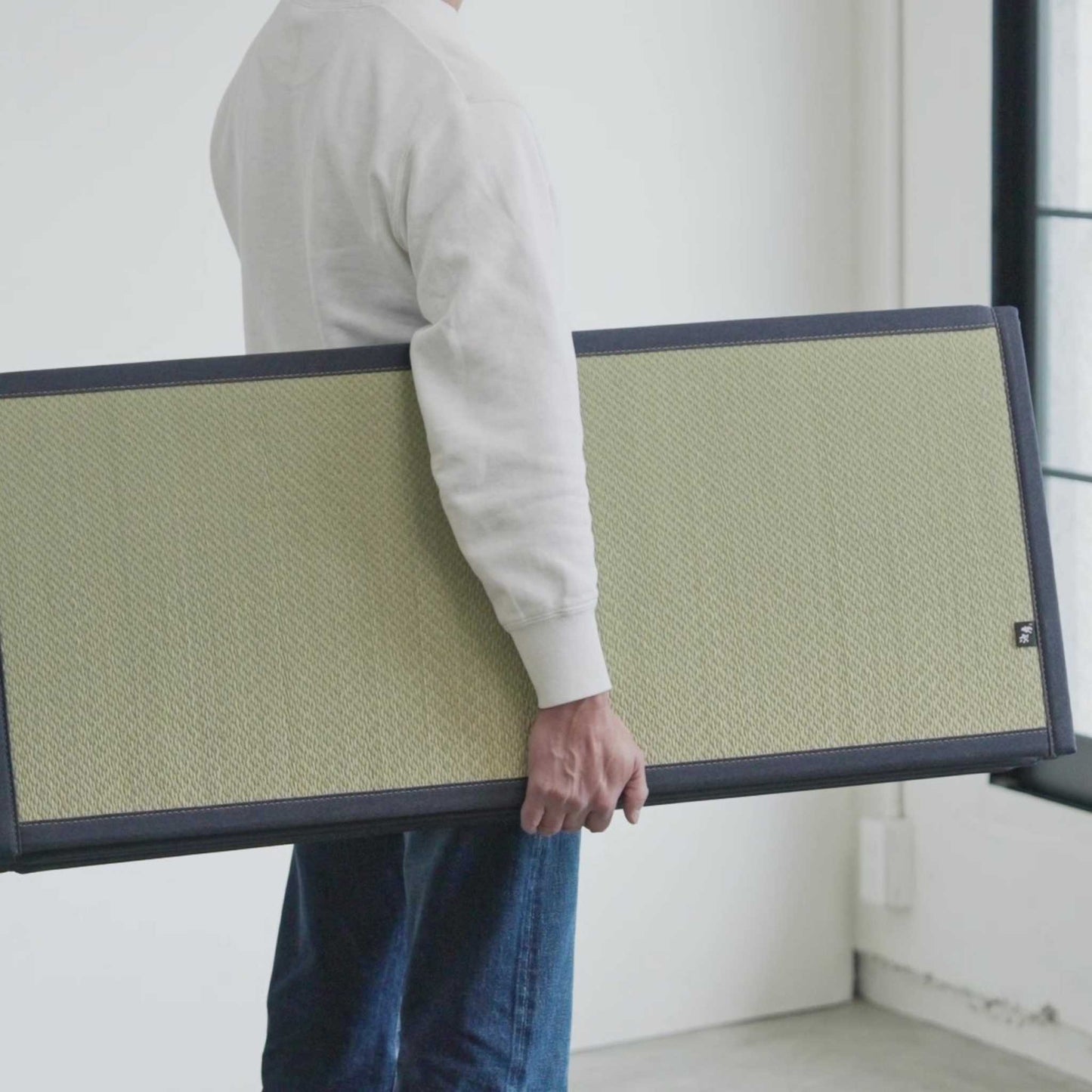 Man carrying a folded lightweight tatami mattress demonstrating its portability and compact storage design.