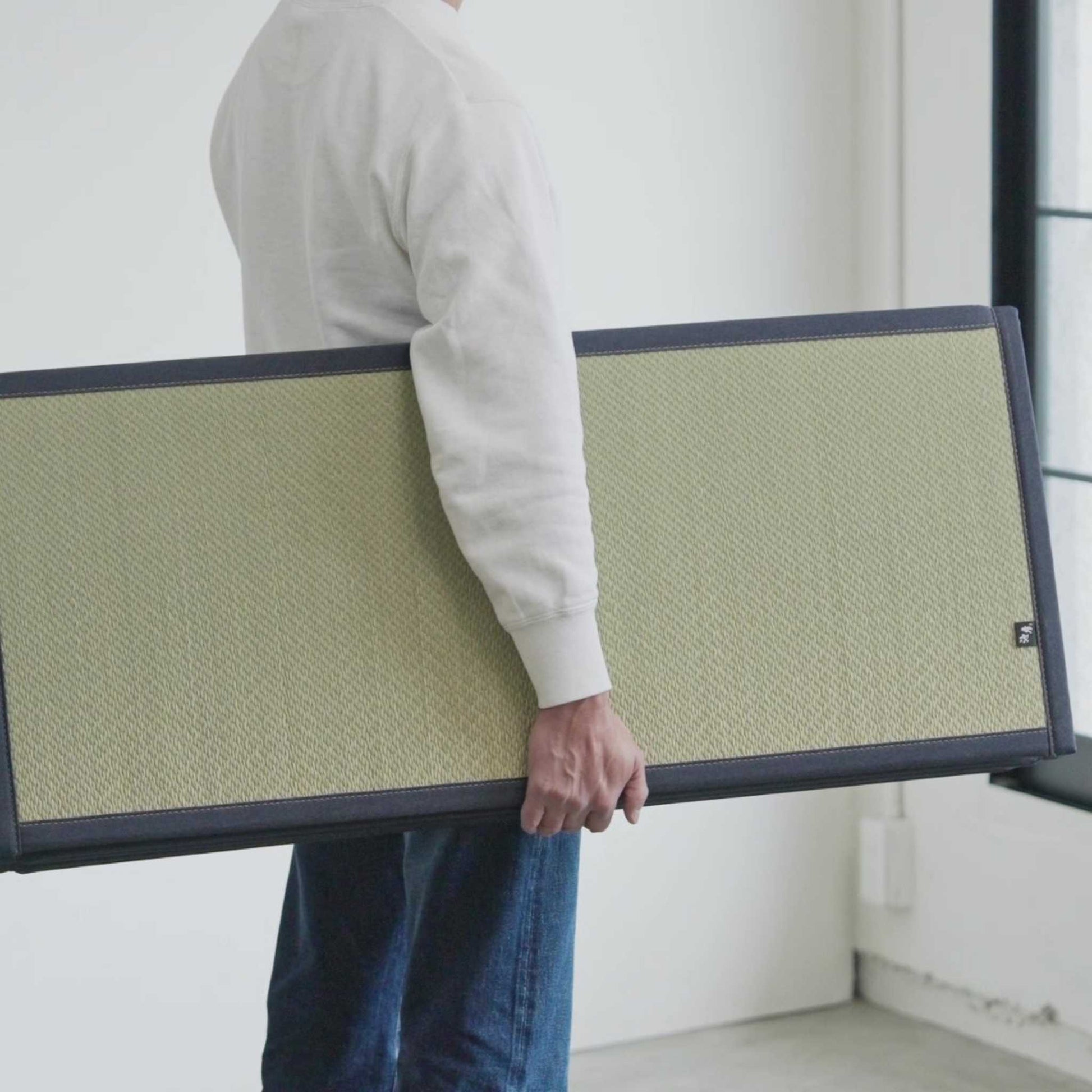 Man carrying a folded lightweight tatami mattress demonstrating its portability and compact storage design.