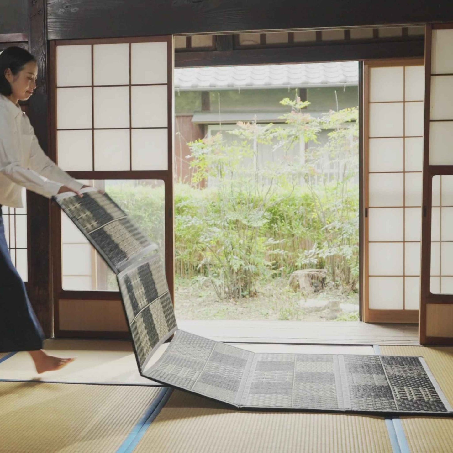 Woman vertically unfolding a five panel tatami mattress showing how easily it transforms a room.