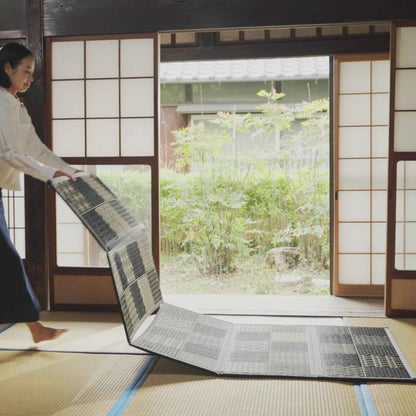 Woman vertically unfolding a five panel tatami mattress showing how easily it transforms a room.