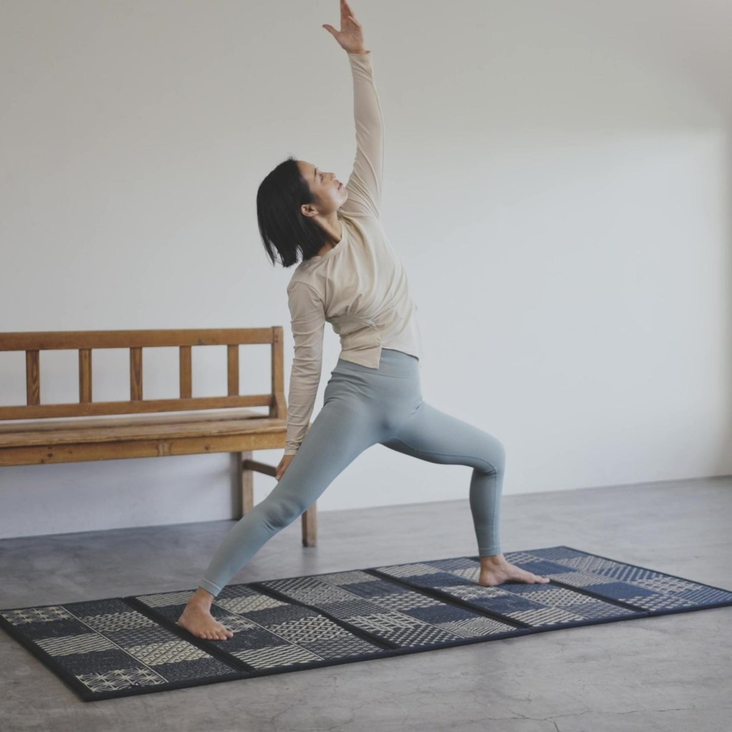 Woman performing a warrior pose on a black tatami mat highlighting stability for yoga and meditation.
