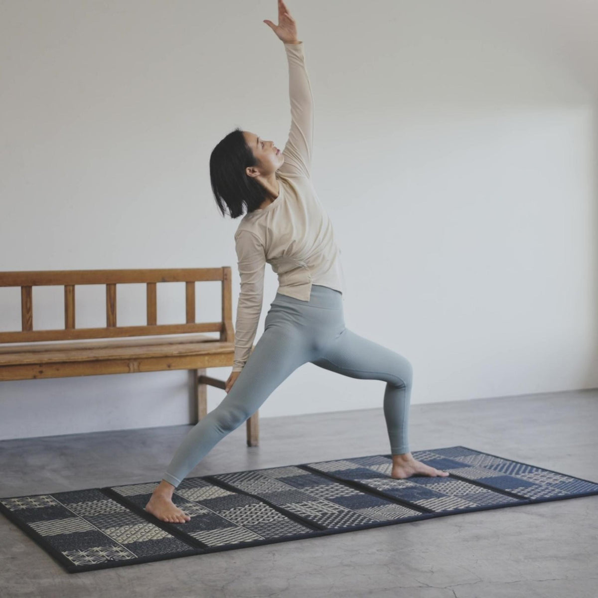 Woman performing a warrior pose on a black tatami mat highlighting stability for yoga and meditation.