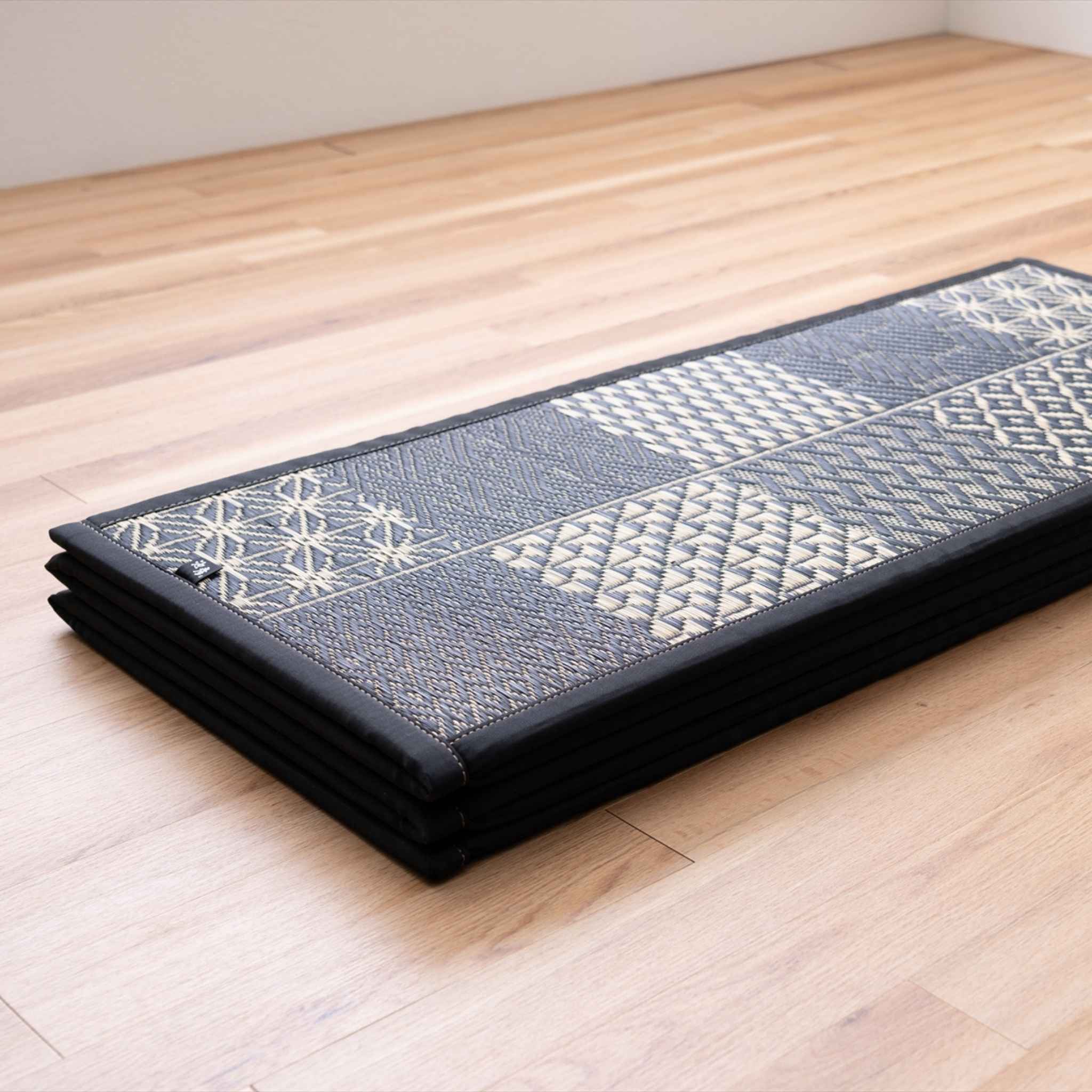 Folded black geometric tatami mat placed on a wooden floor showing its compact storage design.