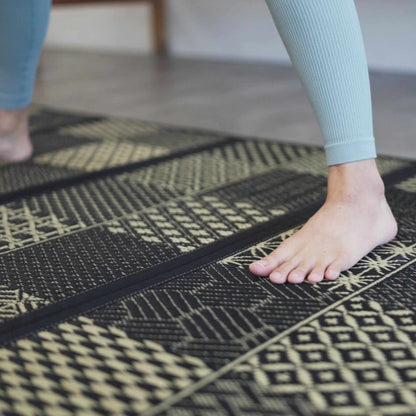 Close up of feet on a black patterned tatami mat showing the woven texture ideal for yoga and barefoot living.