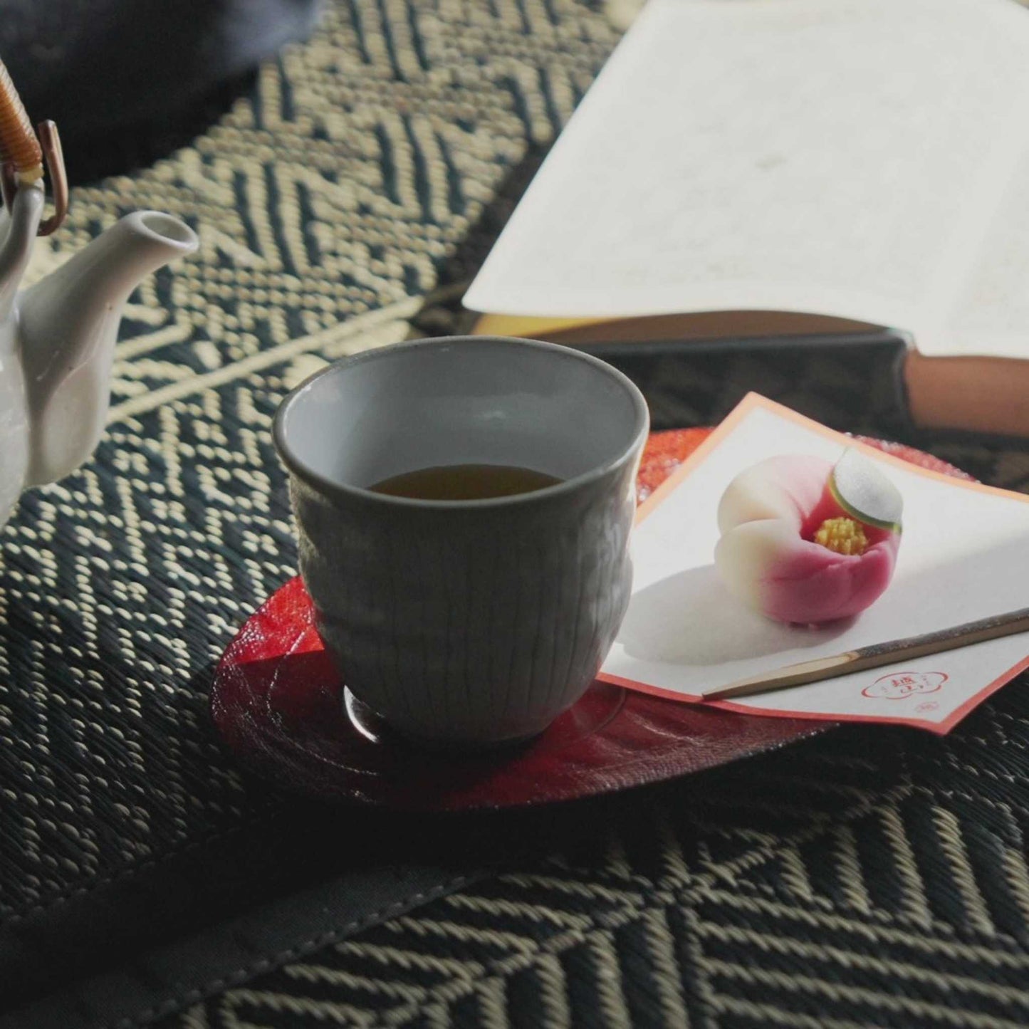 Japanese tea cup and sweet placed on a black geometric tatami mat for a peaceful zen break.