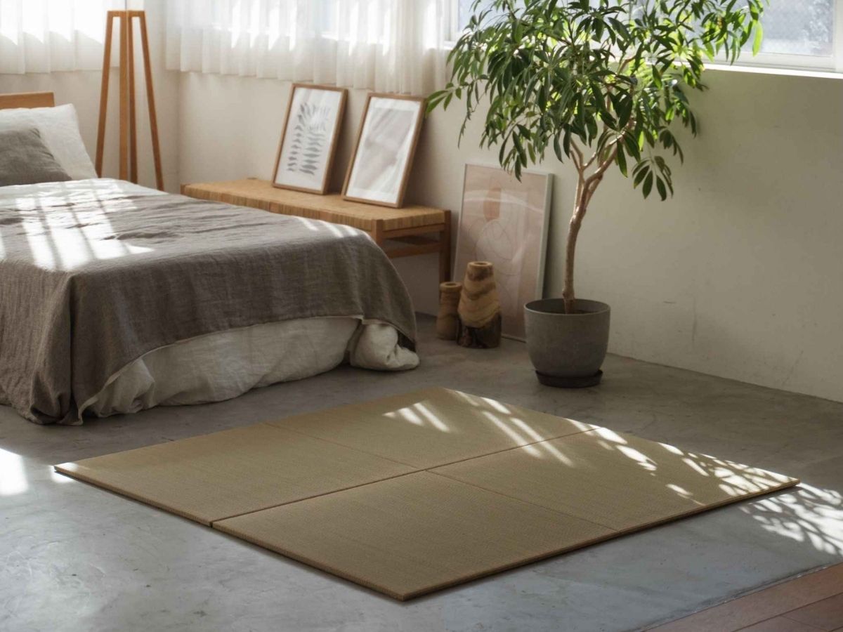 Square unit tatami mats arranged as a rug on a concrete bedroom floor defining a calm meditation space.
