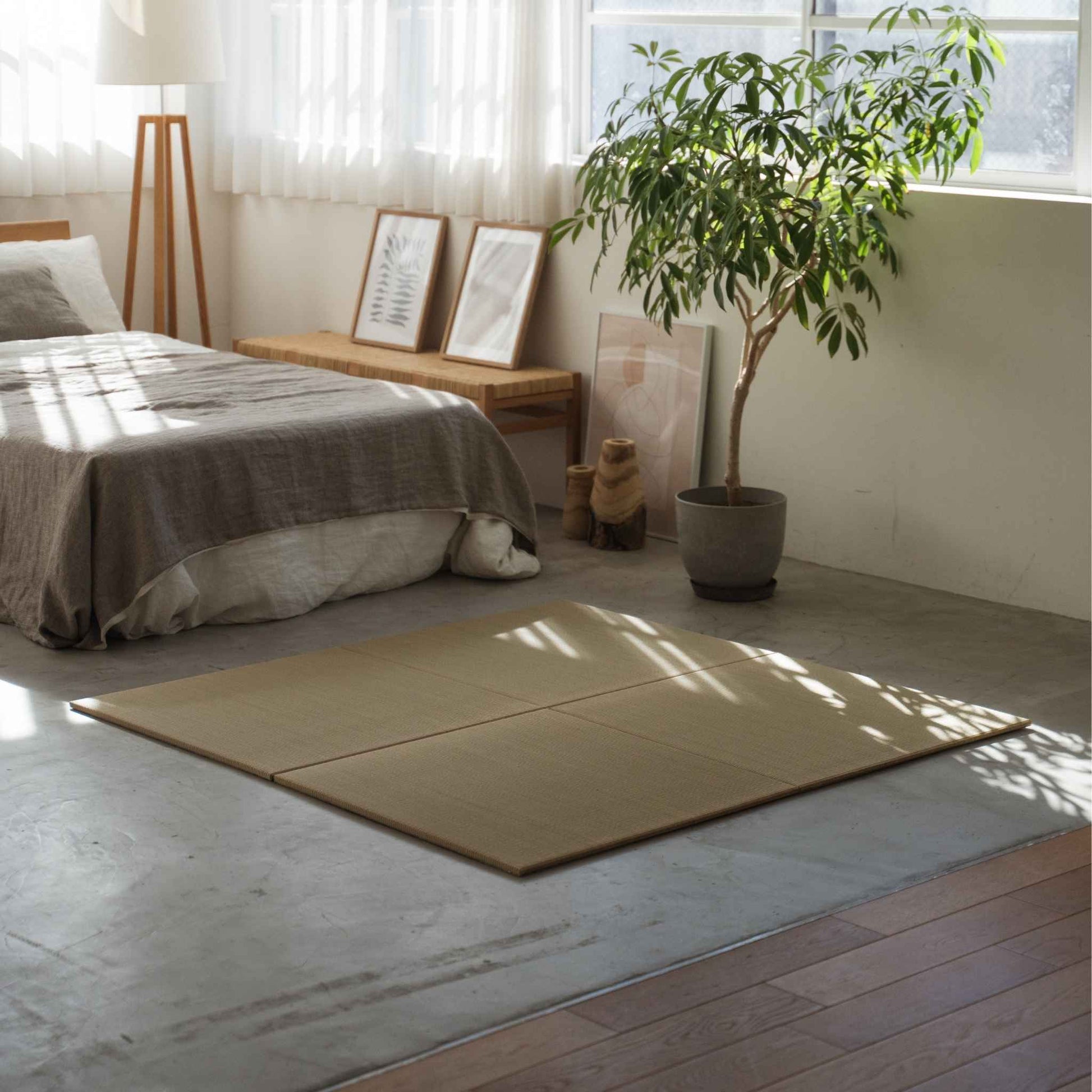 Square unit tatami mats arranged as a rug on a concrete bedroom floor defining a calm meditation space.