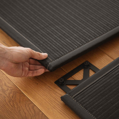 Hands assembling two black square tatami mats on a wooden floor demonstrating easy setup for a zen space.