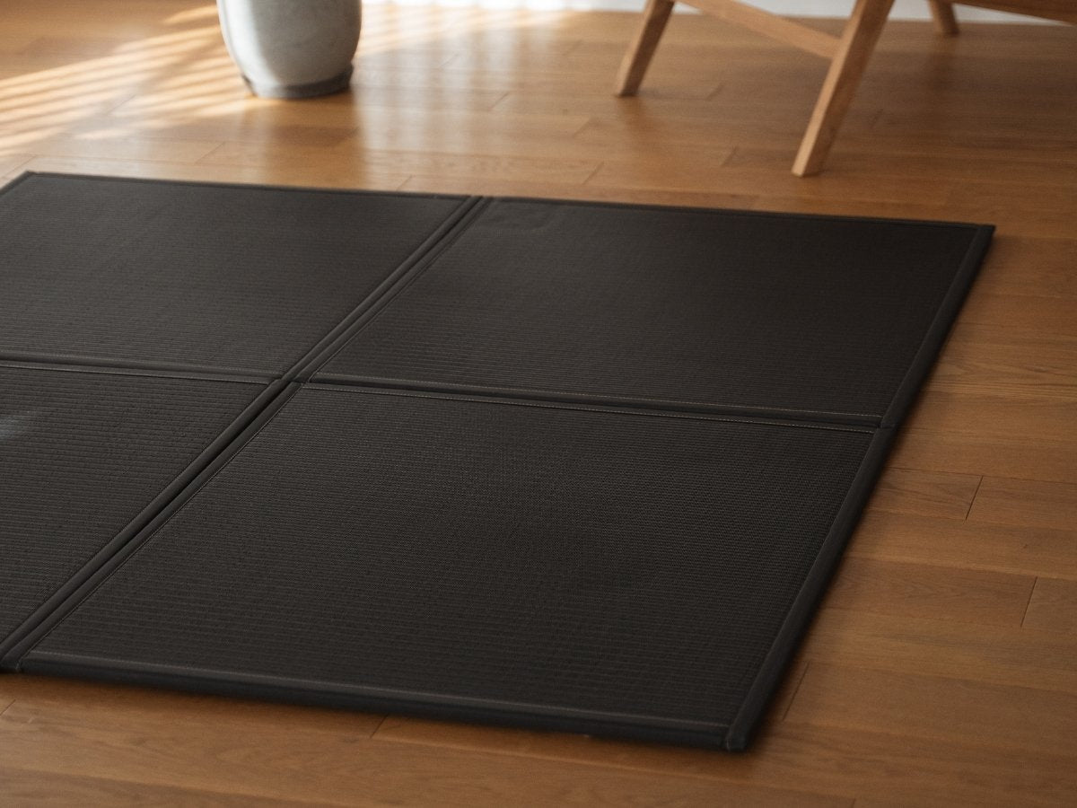 Four black unit tatami mats arranged on a Japandi living room floor serving as a modern and durable zen decor rug.