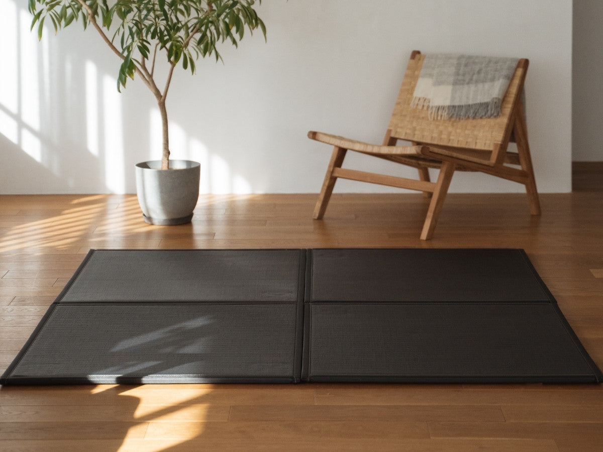 Four black unit tatami mats arranged on a living room floor serving as a modern and durable zen decor rug.
