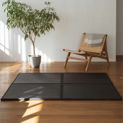 Four black unit tatami mats arranged on a living room floor serving as a modern and durable zen decor rug.