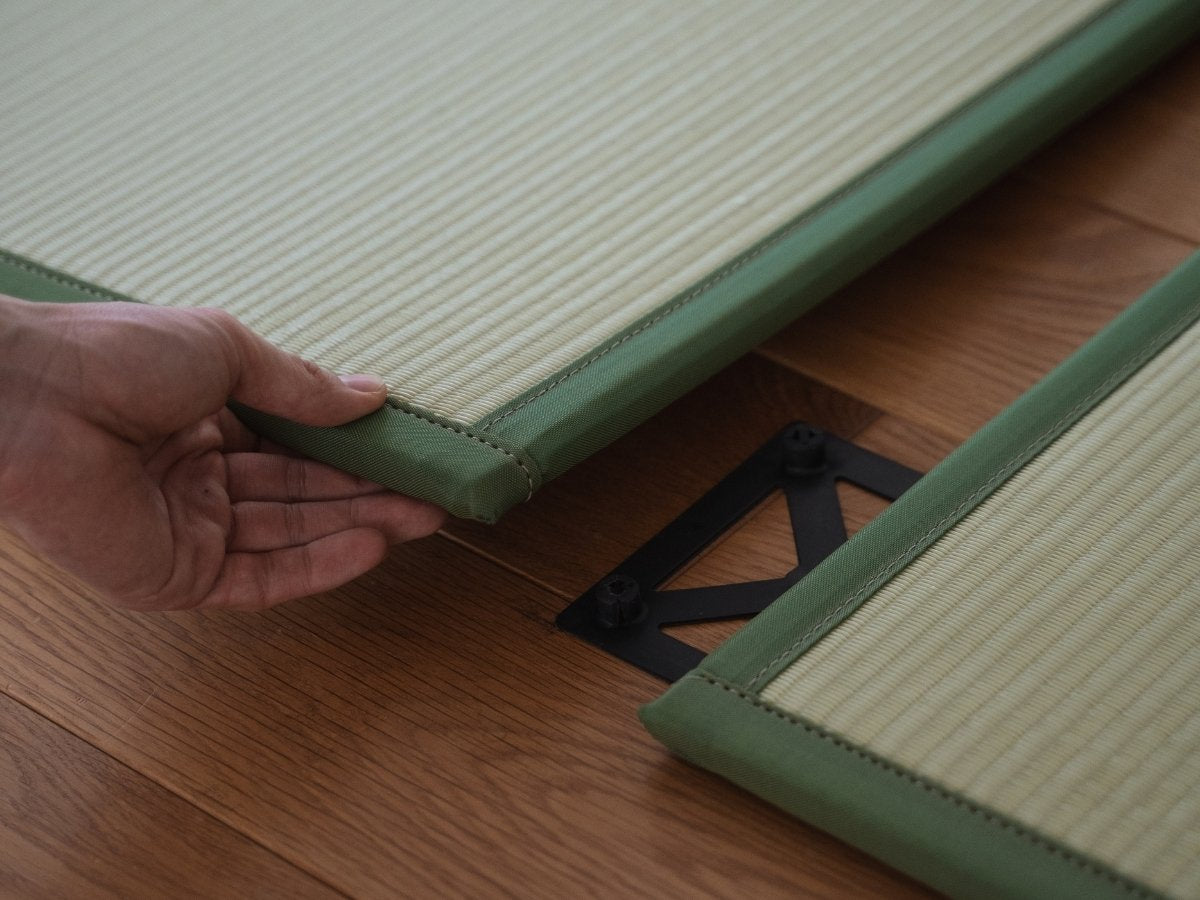 Hands connecting two green tatami mat panels on a floor demonstrating easy setup for a custom Japanese space.