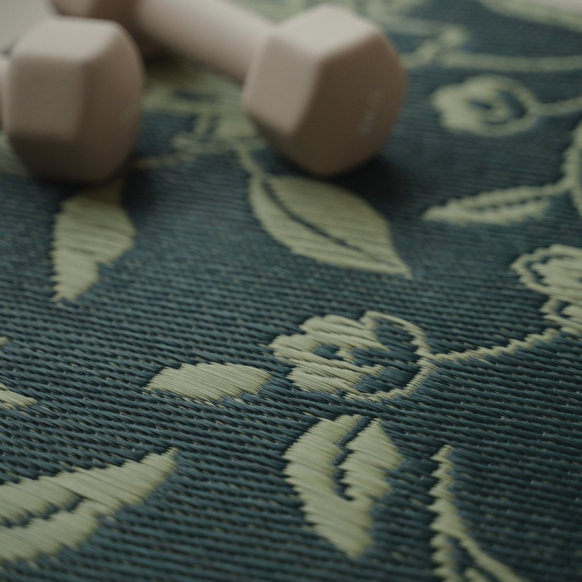 Close-up van het ingewikkelde botanische motief op een Japanse Tatami Yoga Mat "Sarasa" Navy met een halter.