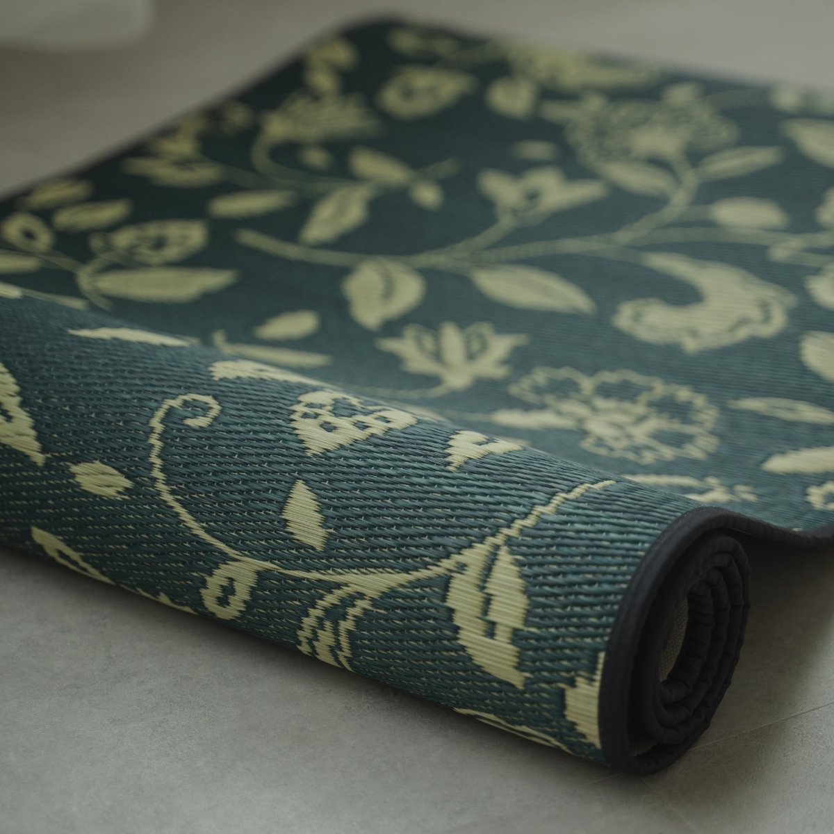 Japanse Tatami Yogamat "Sarasa" Navy gedeeltelijk opgerold op een grijze vloer, met de natuurlijke matgras weving en patroon.