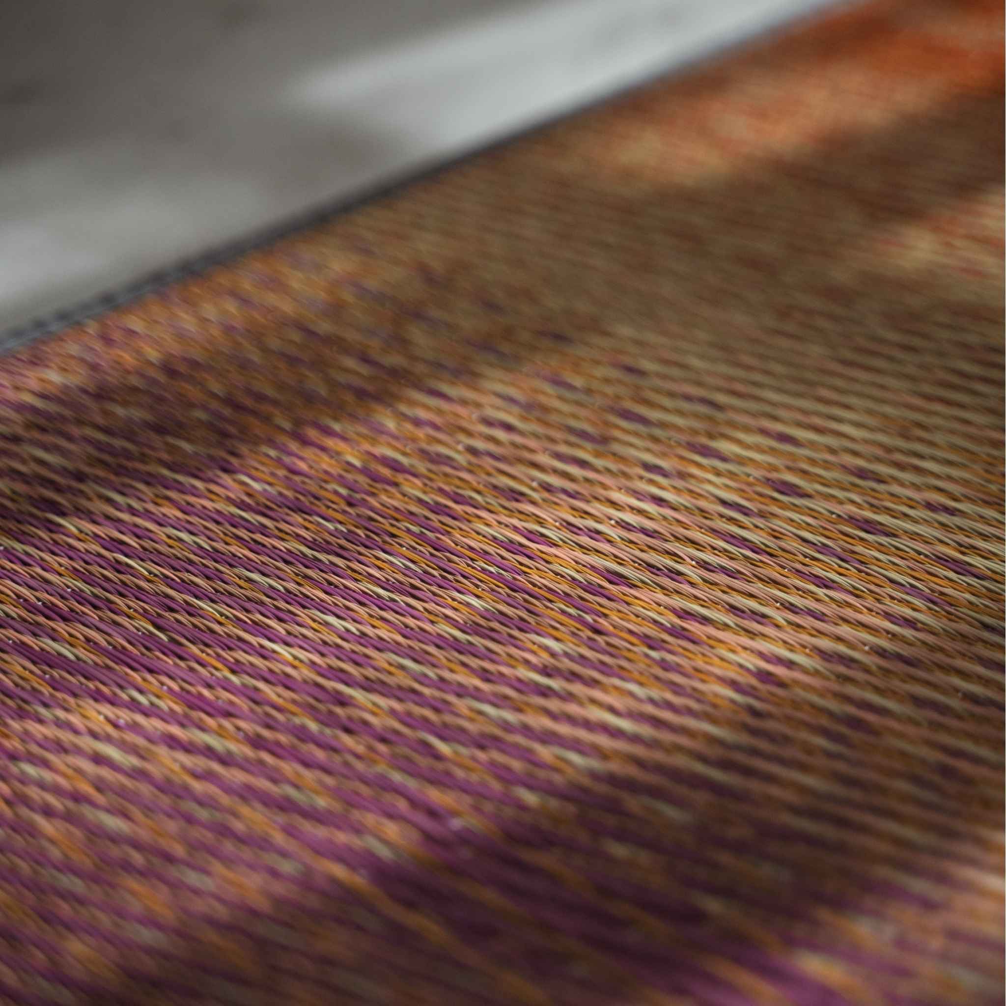 Close up of woven rush grass on a red tatami mat showing the sunset color gradient.
