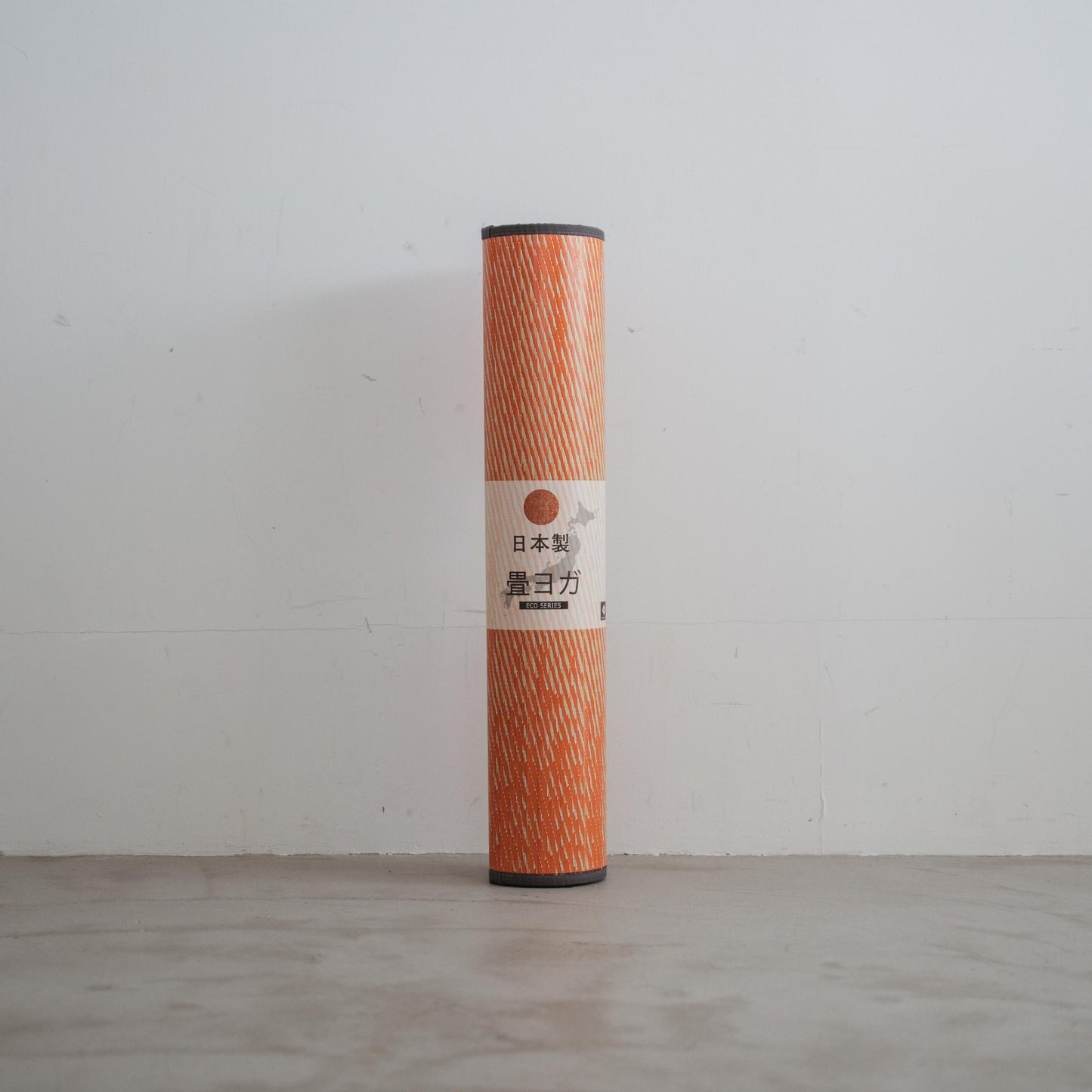 Rolled up red tatami yoga mat standing against a wall highlighting its portable design and Japanese origin.