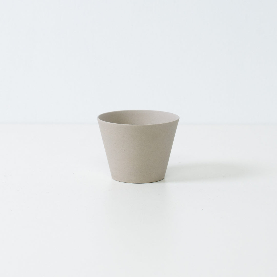Minimalist white japanese tea cup in ensui cone shape made from unglazed stoneware standing on a white table.