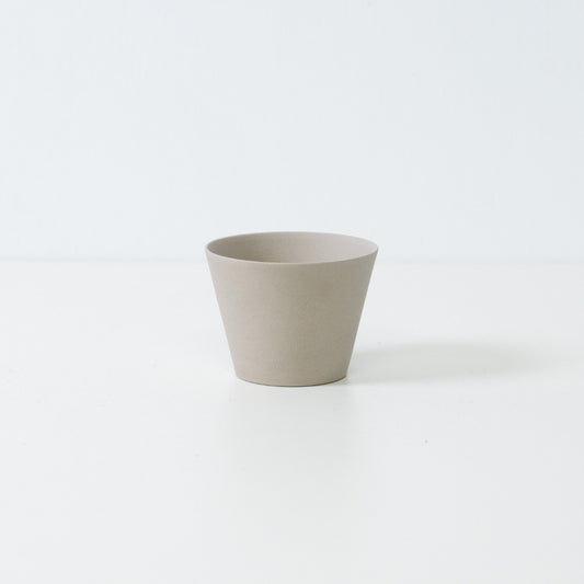 Minimalist white japanese tea cup in ensui cone shape made from unglazed stoneware standing on a white table.