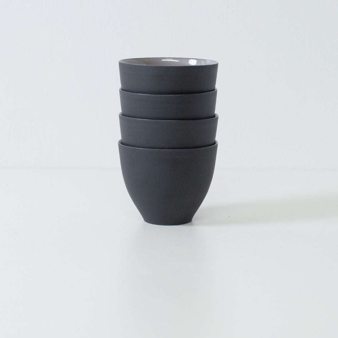 Stack of four black japanese tea cups forming a compact modern japanese tea set ready for storage