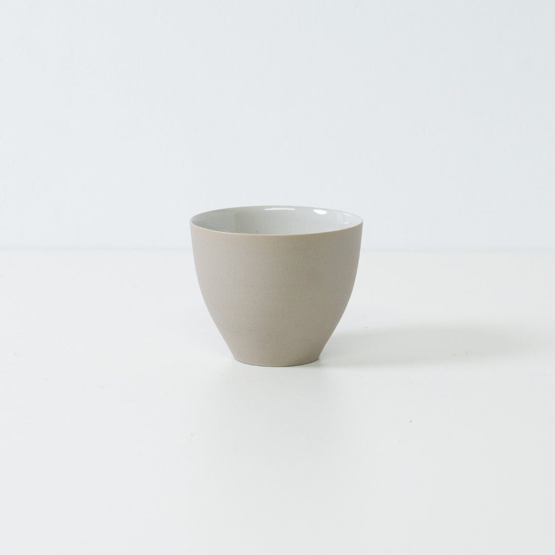 Side view of a single modern f shape japanese tea cup showing its curved unglazed white exterior and stable base