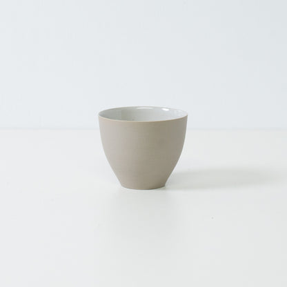 Side view of a single modern f shape japanese tea cup showing its curved unglazed white exterior and stable base