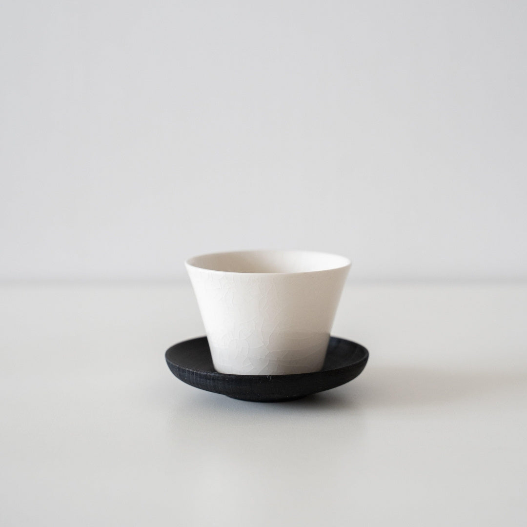 A single high-footed Japanese tea cup resting on a dark saucer, highlighting the elegant wabi-sabi porcelain finish.