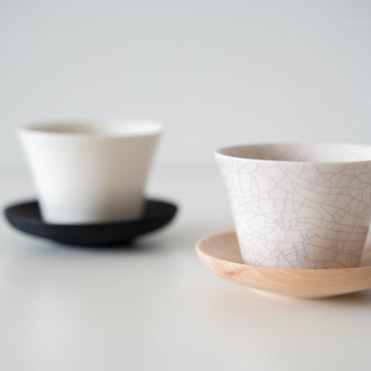 Two Kodai Japanese tea cups on wood and black saucers focusing on the intricate Kannyu crackle glaze pattern details.